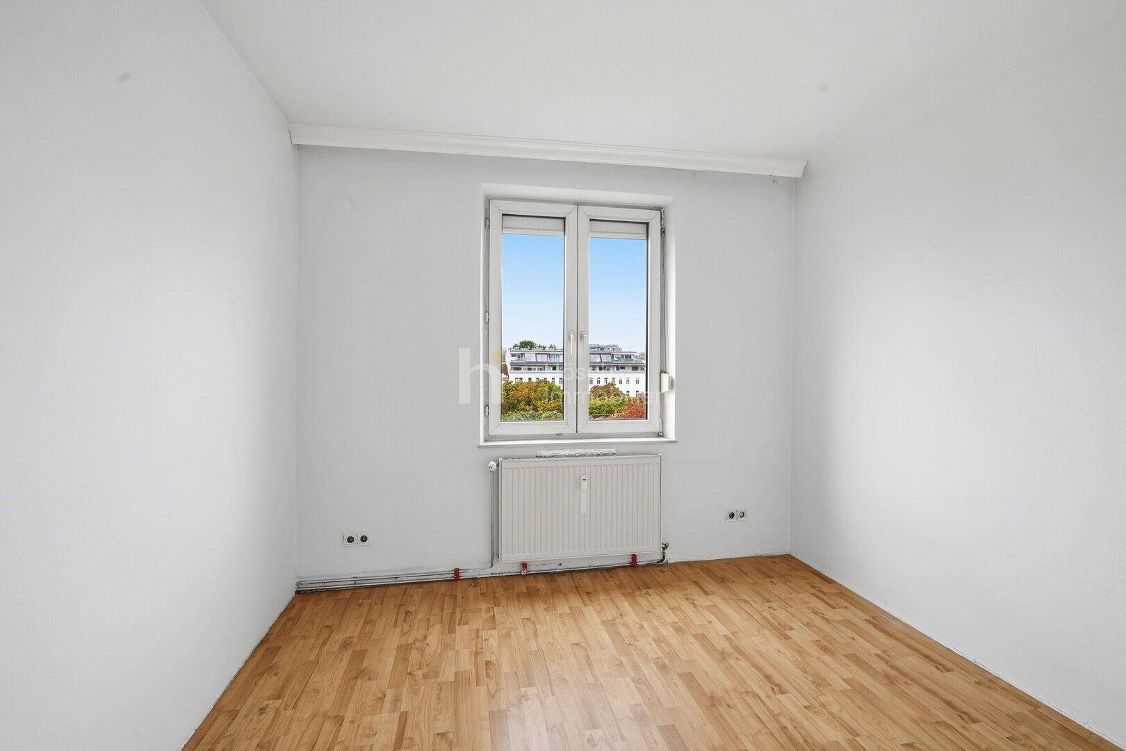 Ruhiges Zimmer mit Parkettboden und einem Fenster, das einen Blick auf die Umgebung freigibt.