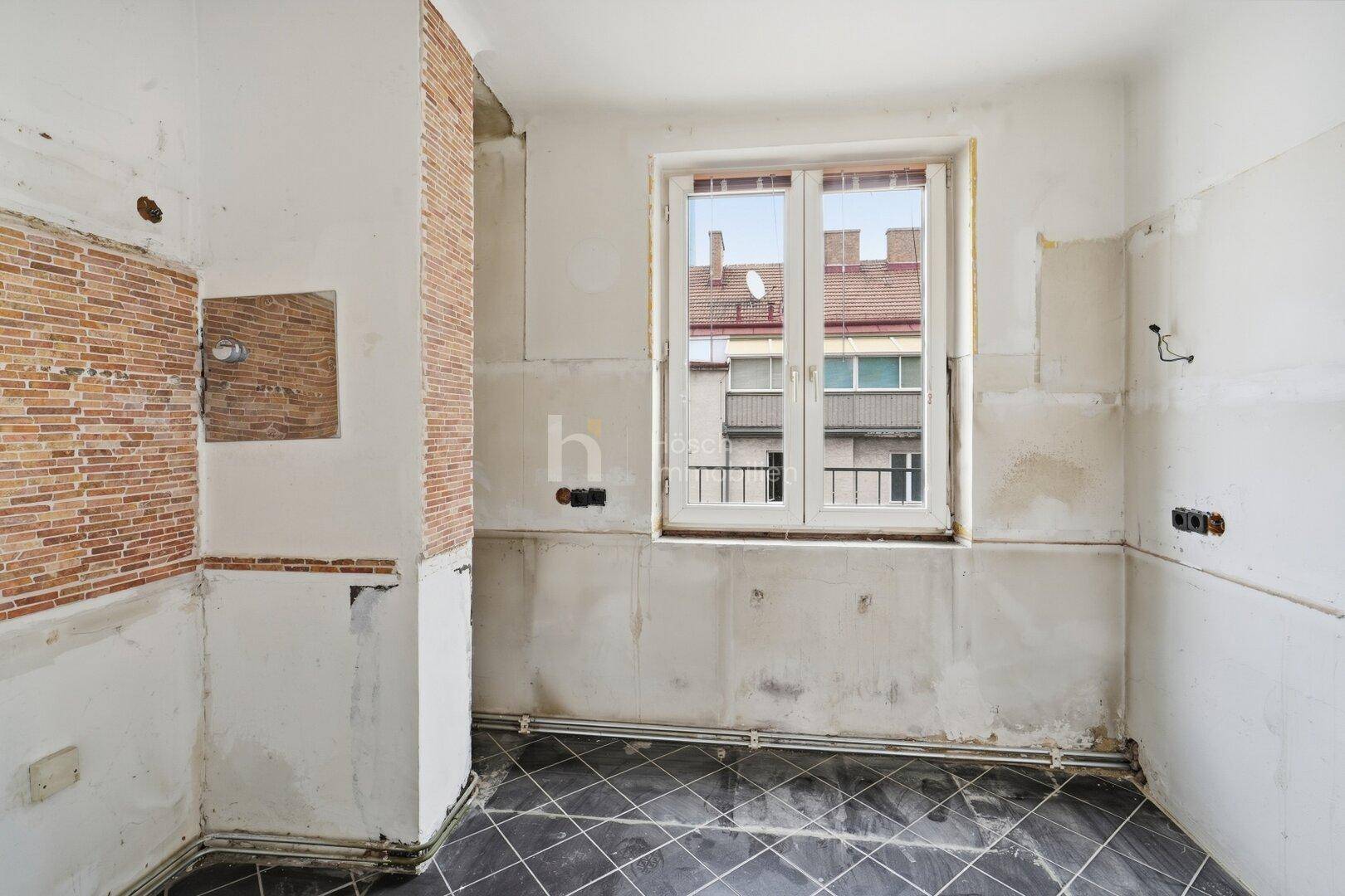 Unfertige Küche mit freiliegenden Ziegelwänden und Fliesenboden, bereit für den Ausbau.