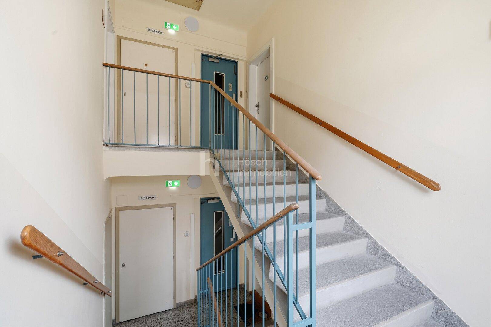 Treppenhaus mit mehreren Etagen, Metallgeländer und sichtbarem Aufzug im Gebäude.