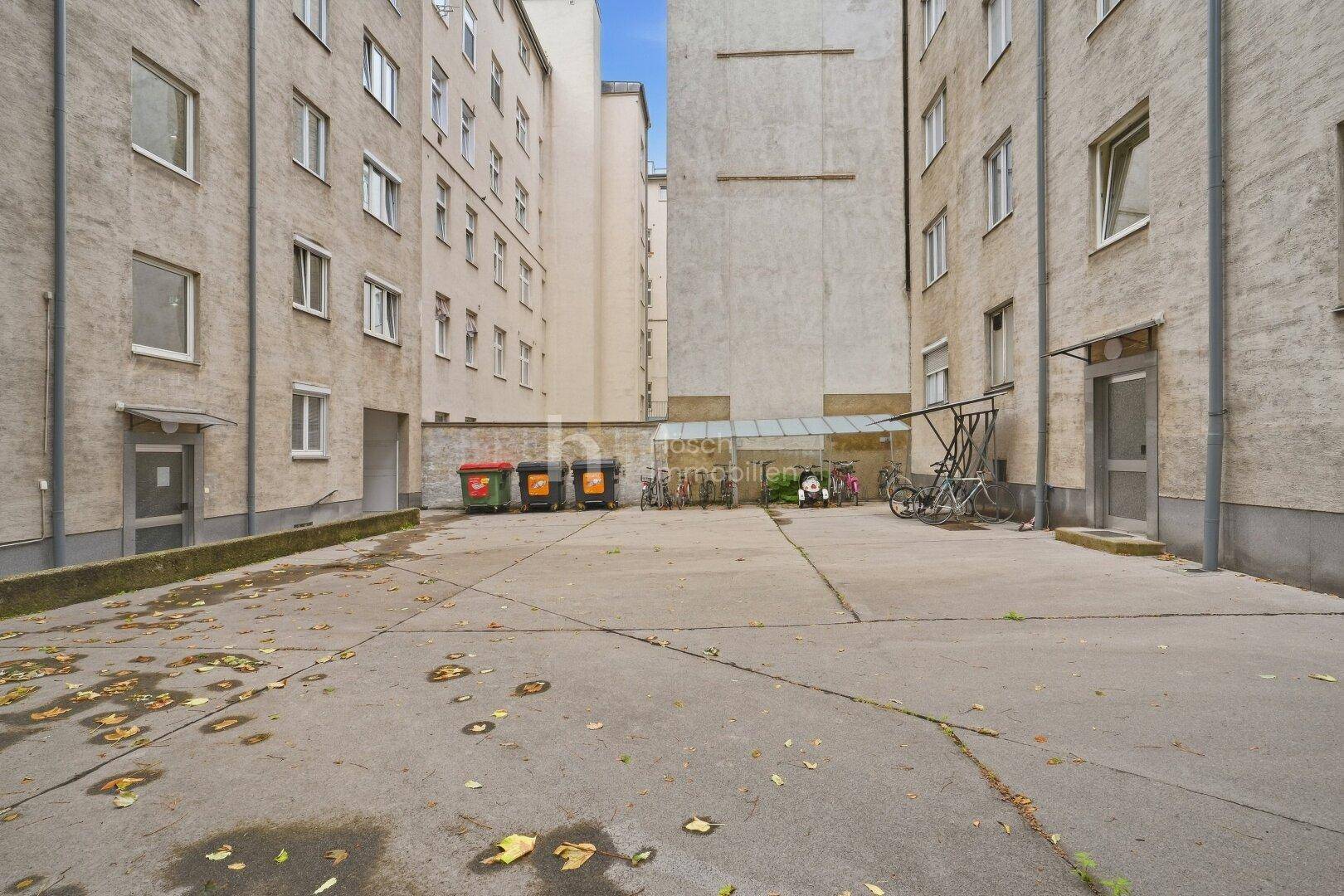 Innenhof zwischen Wohngebäuden mit Abfallbehältern und Fahrradständern.