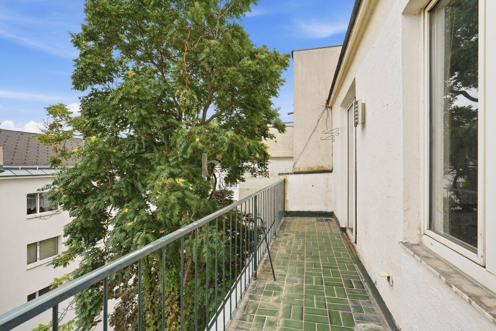 Schmaler Balkon mit grünen Fliesen und Metallgeländer, umgeben von üppigem Grün.