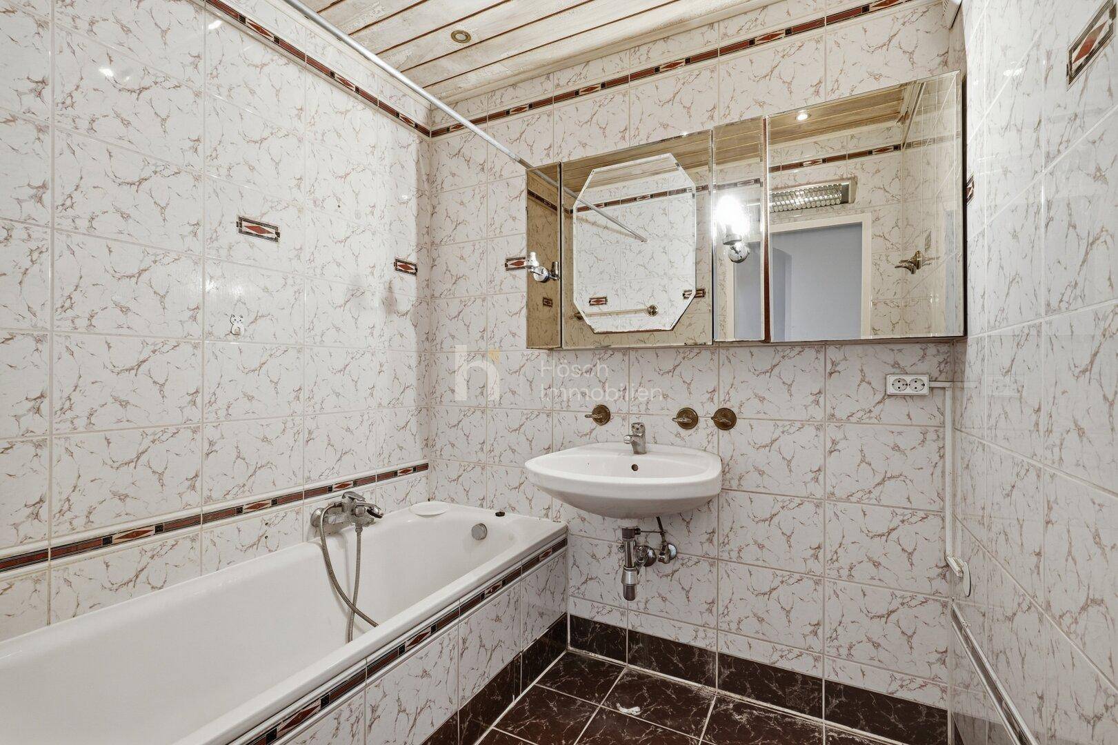 Gefliestes Badezimmer mit Badewanne, Waschbecken und Spiegelschrank.