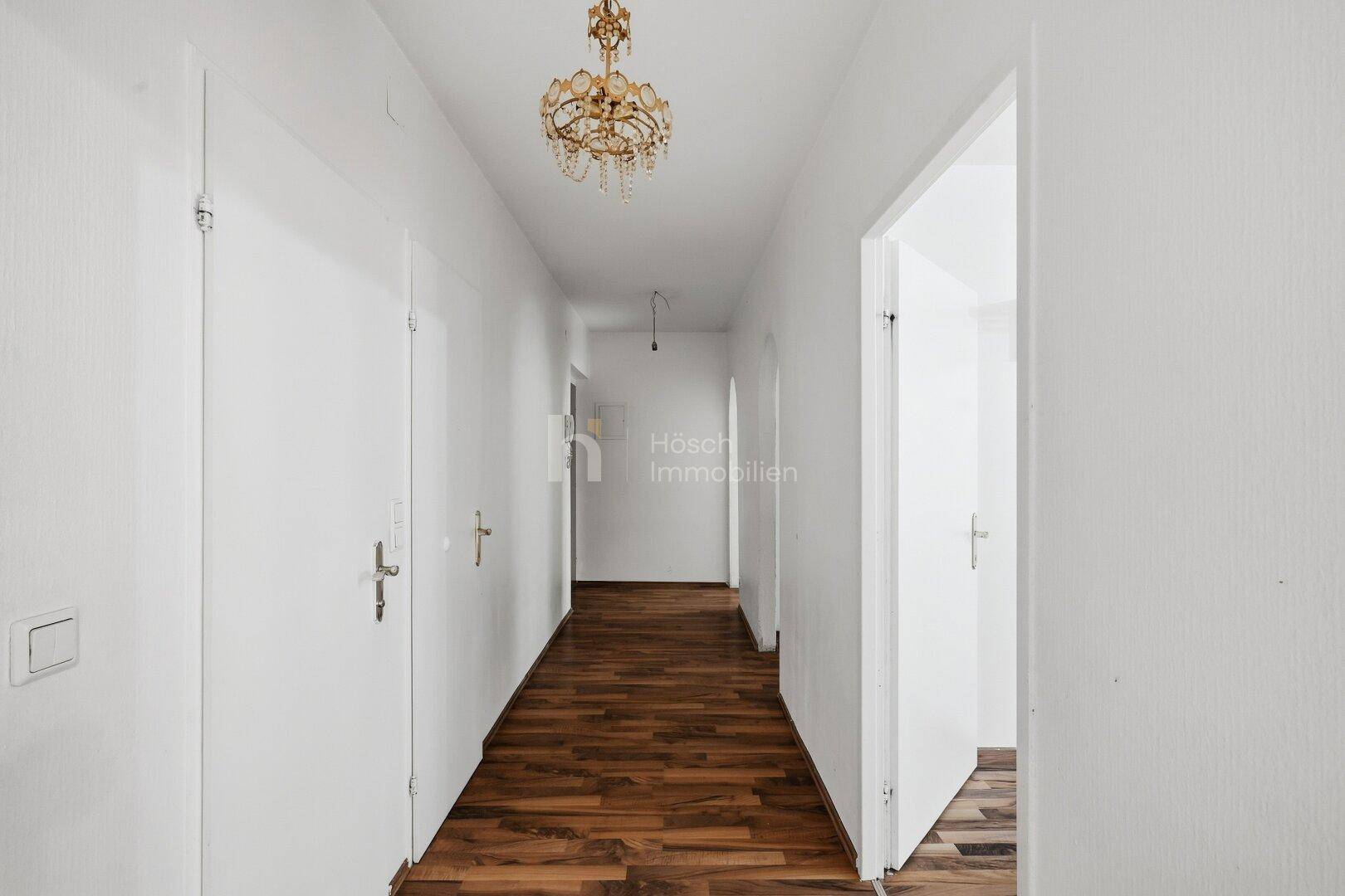 Heller Flur mit Laminatboden und Kronleuchter, der zu den Zimmern führt.