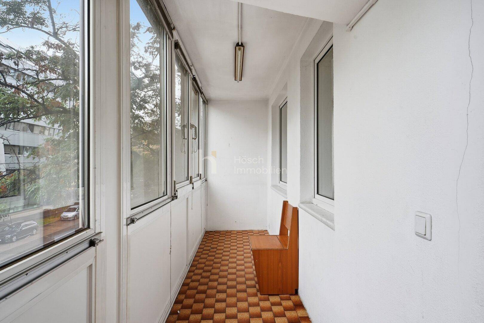 Verglaste Loggia mit Fliesenboden und Blick ins Grüne.