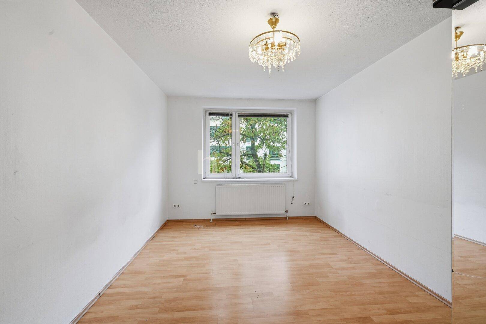 Helles Zimmer mit Laminatboden, Kronleuchter und Blick ins Grüne.