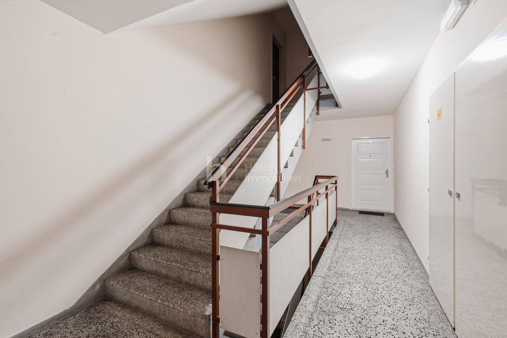 Treppenhaus mit Steinstufen und Geländer in einem Mehrfamilienhaus.