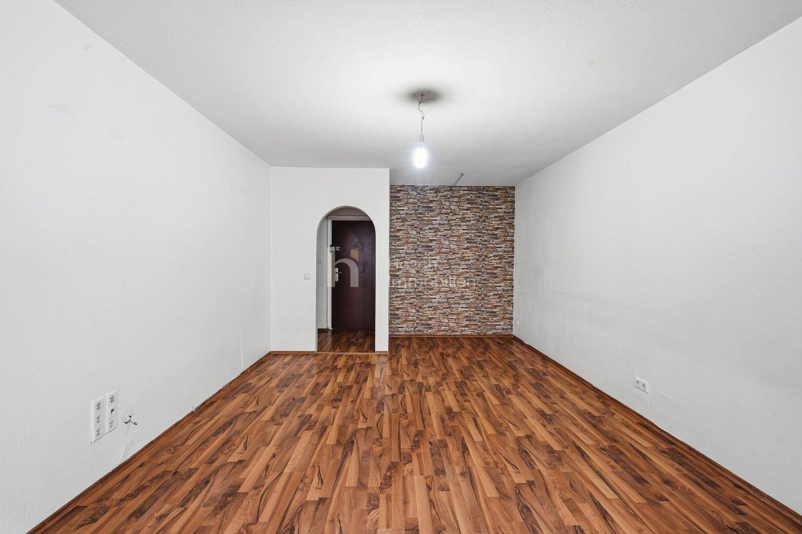 Geräumiges Wohnzimmer mit Laminatboden und einer Akzentwand in Steinoptik.