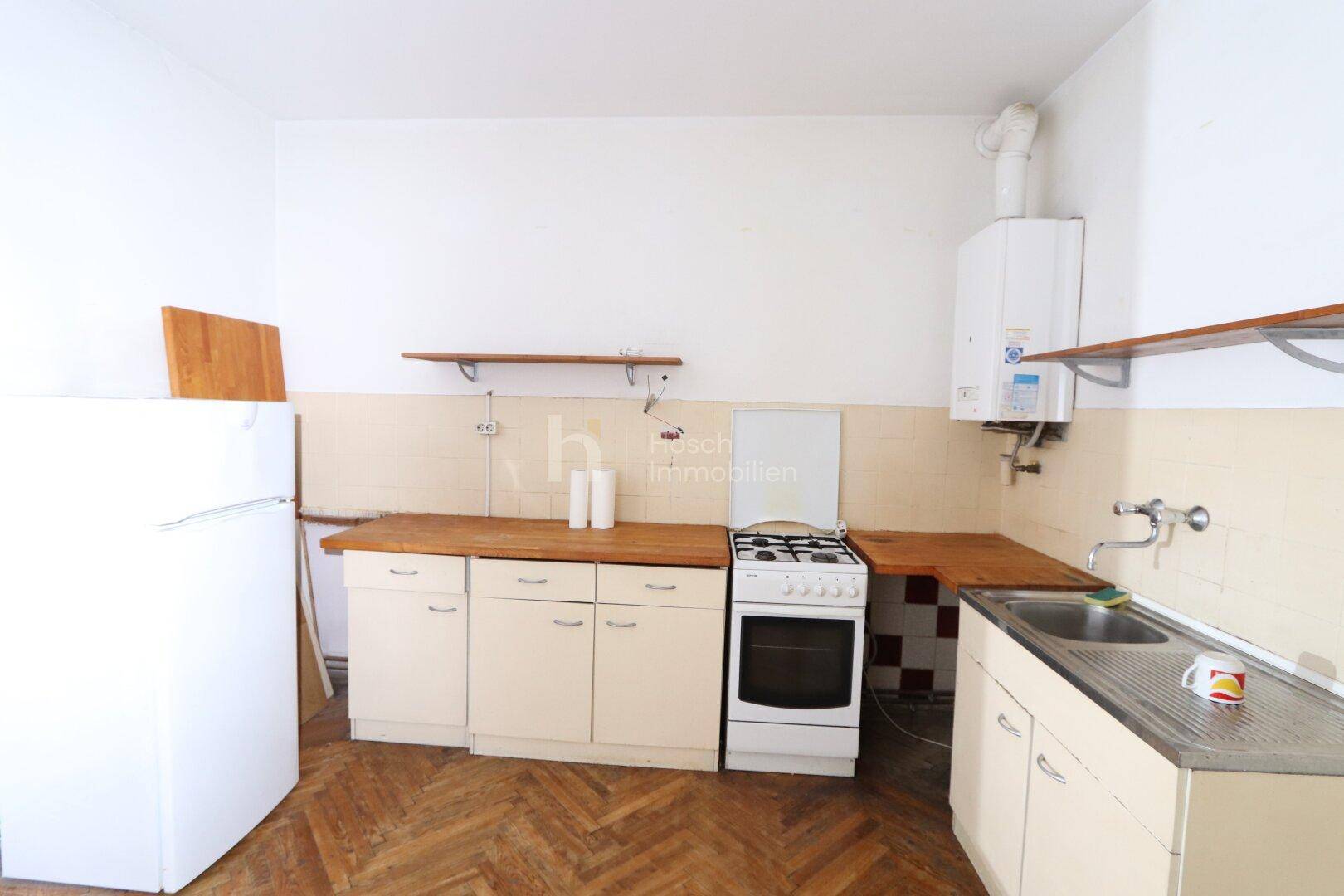 Funktionale Küche mit älteren Einbauschränken, Gasherd und einem Wandboiler, bereit zur Modernisierung.