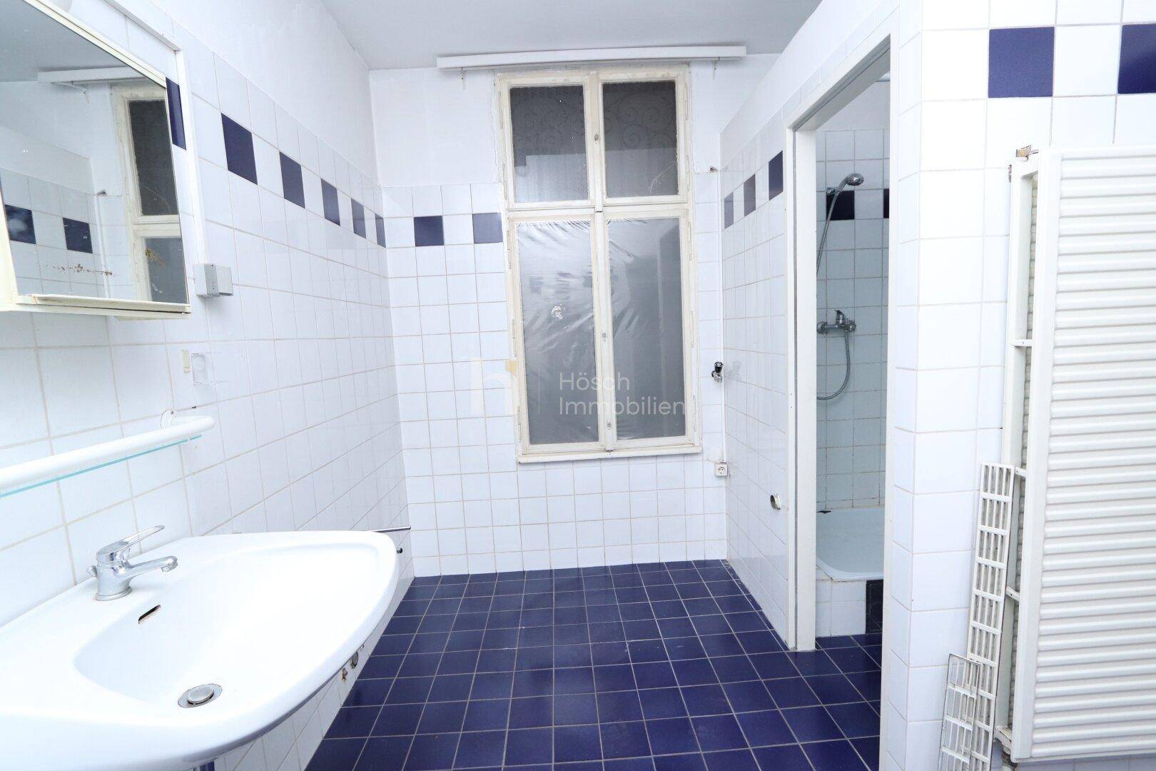 Badezimmer mit weißen und blauen Fliesen, Einzelwaschbecken, Fenster und einer Duschwanne.
