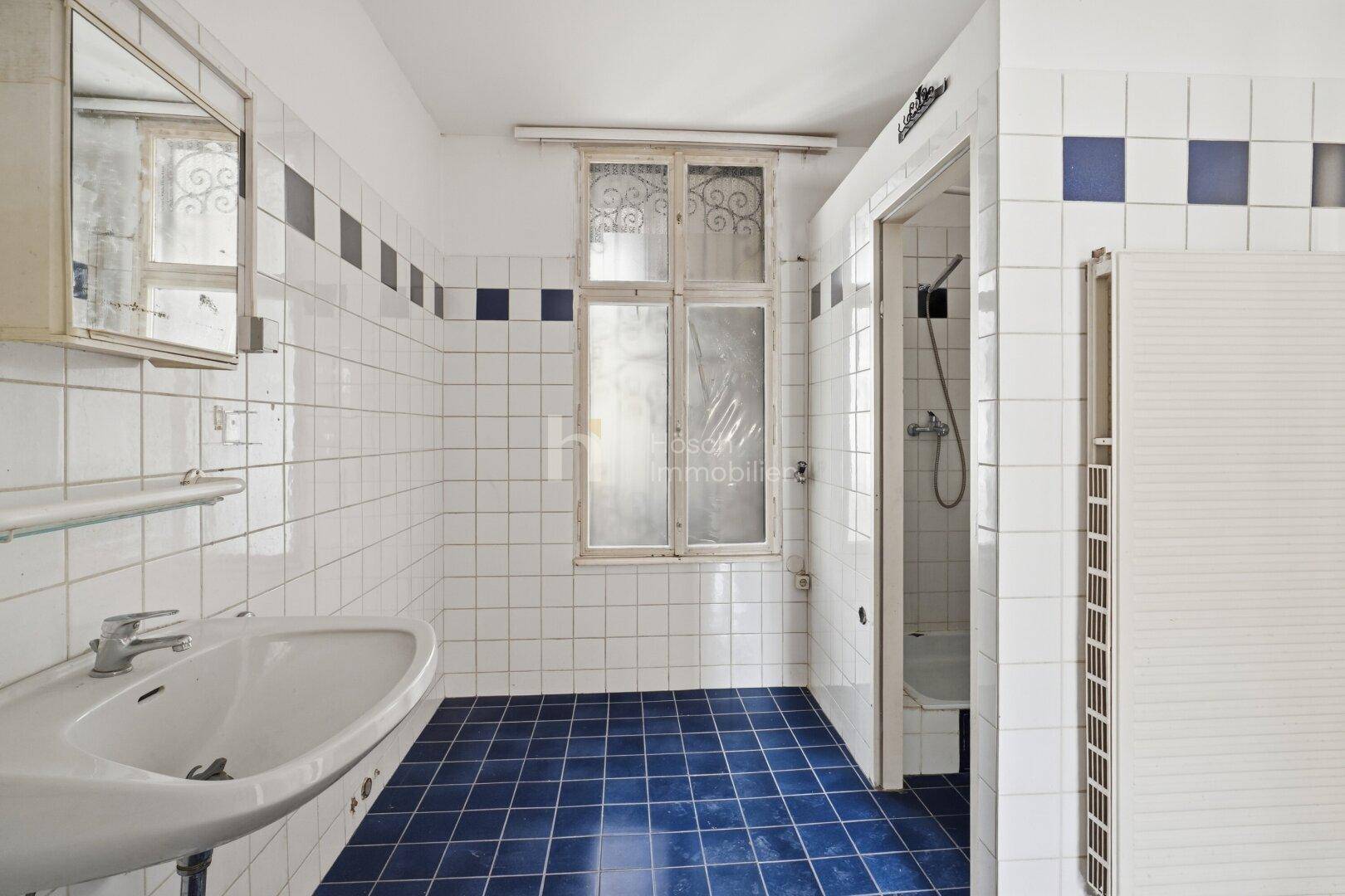 Badezimmer mit blauen und weißen Fliesen, Waschbecken und Duschkabine, ausgestattet mit einem Fenster.