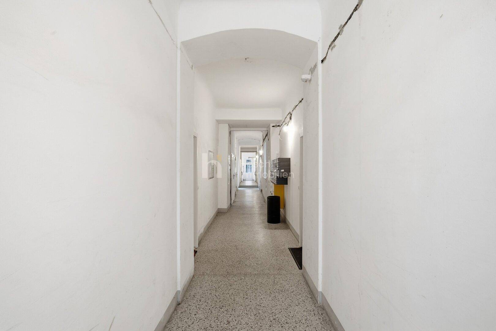 Langer, schmaler Flur mit Terrazzoboden und weiß gestrichenen Wänden in einem Altbau.