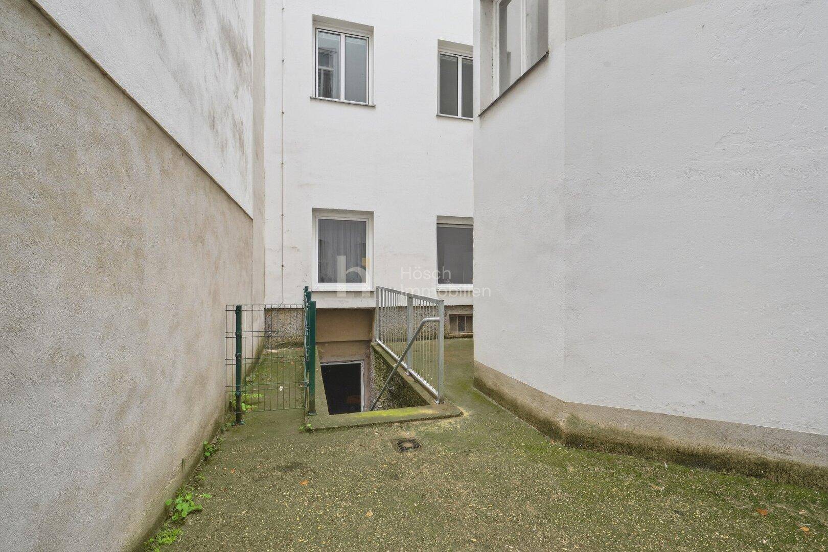 Hinterhofbereich mit Zugang zum Keller über eine Treppe und hohen Gebäudewänden.