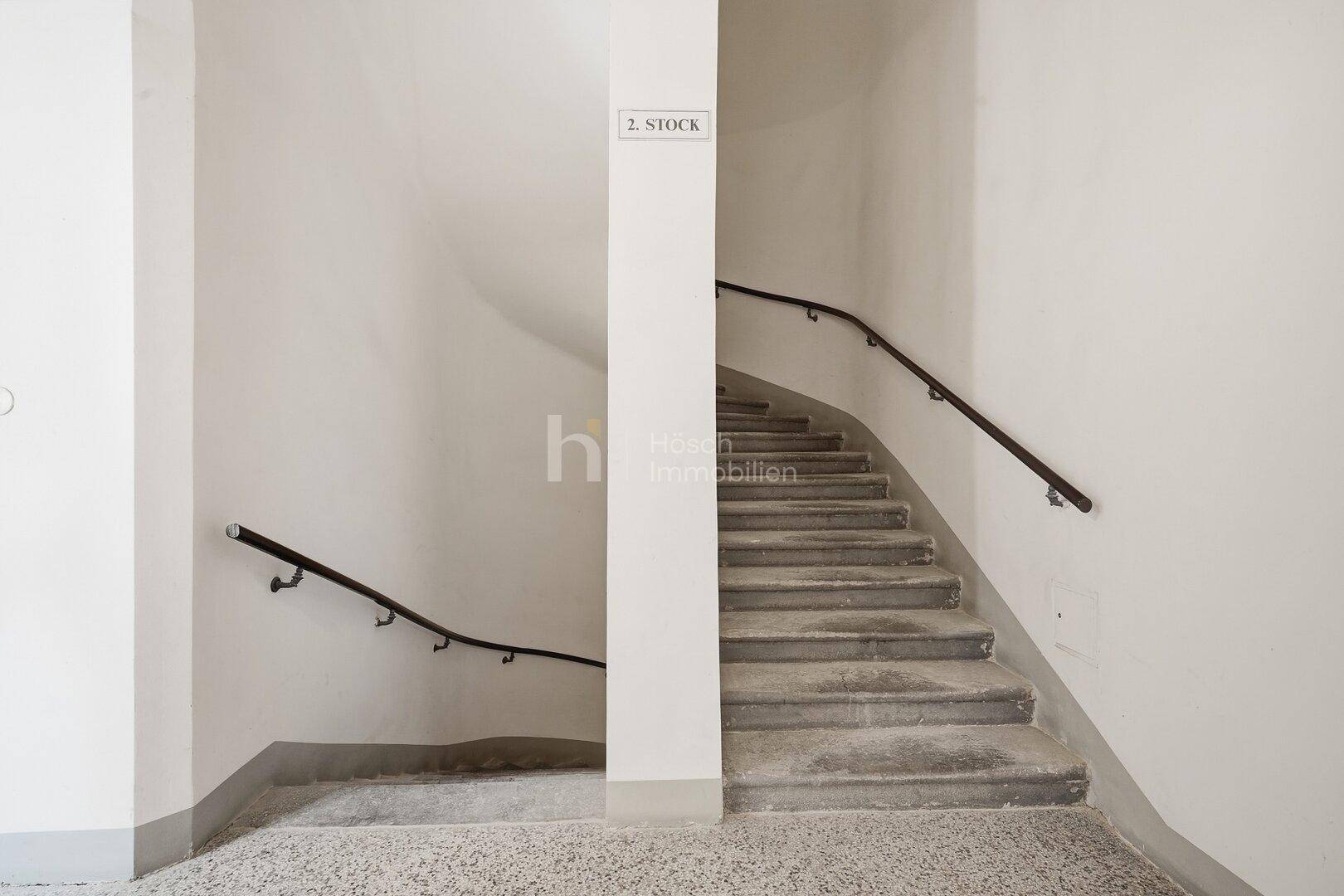 Treppenhaus mit Steinstufen und schlichten Handläufen, das in die oberen Stockwerke führt.