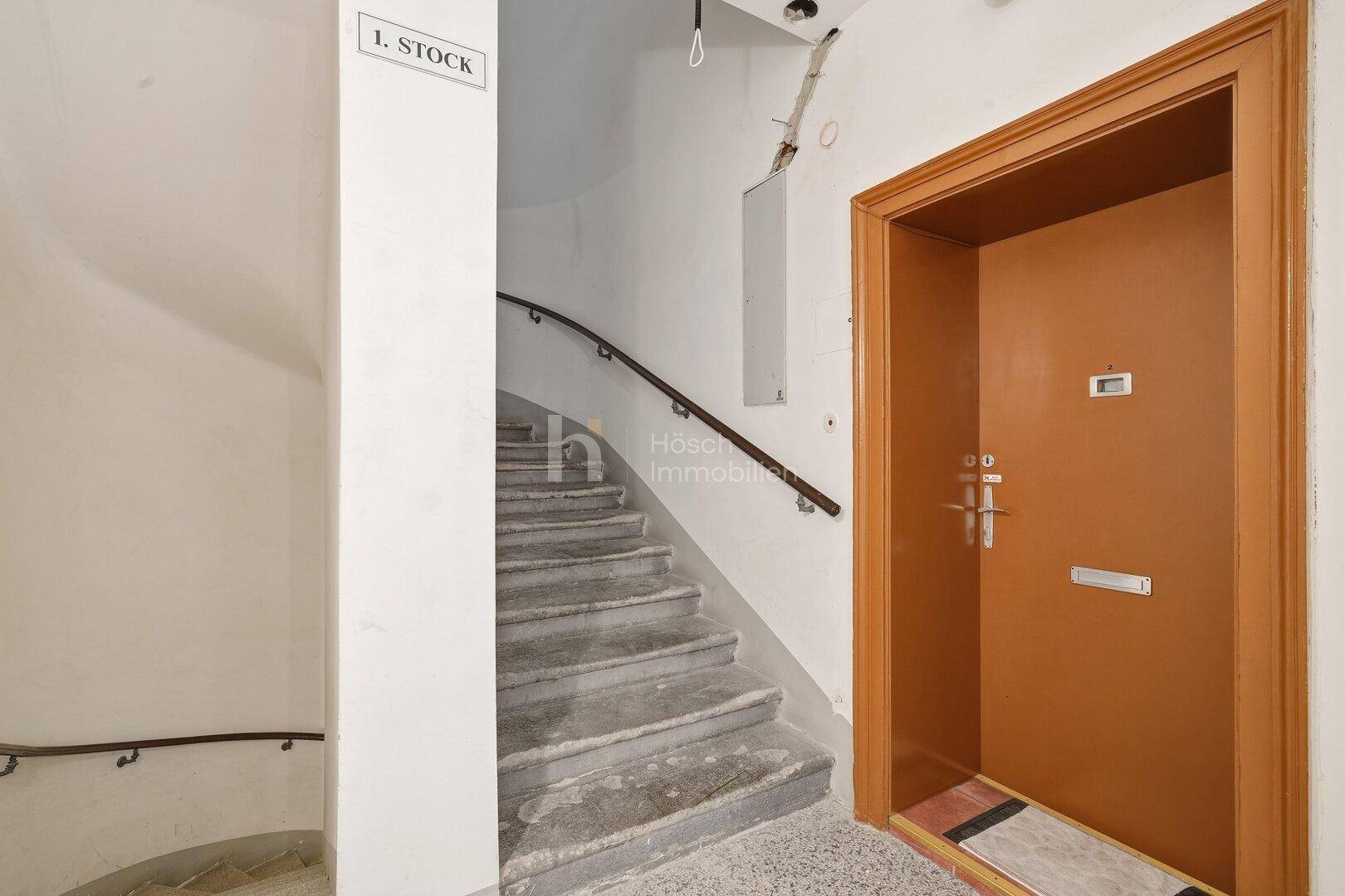 Treppenhaus mit Steinstufen und einer braunen Wohnungstür im ersten Stock.