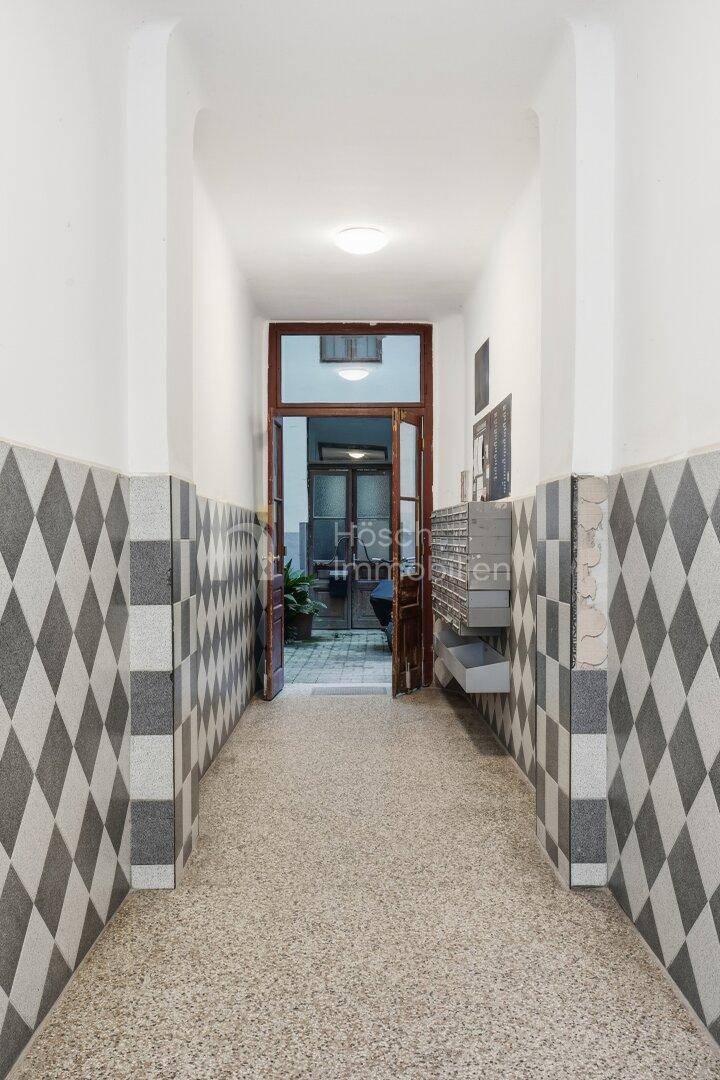 Eingangsbereich mit gemusterten Fliesenwänden, Terrazzoboden und Briefkästen an der Seite.