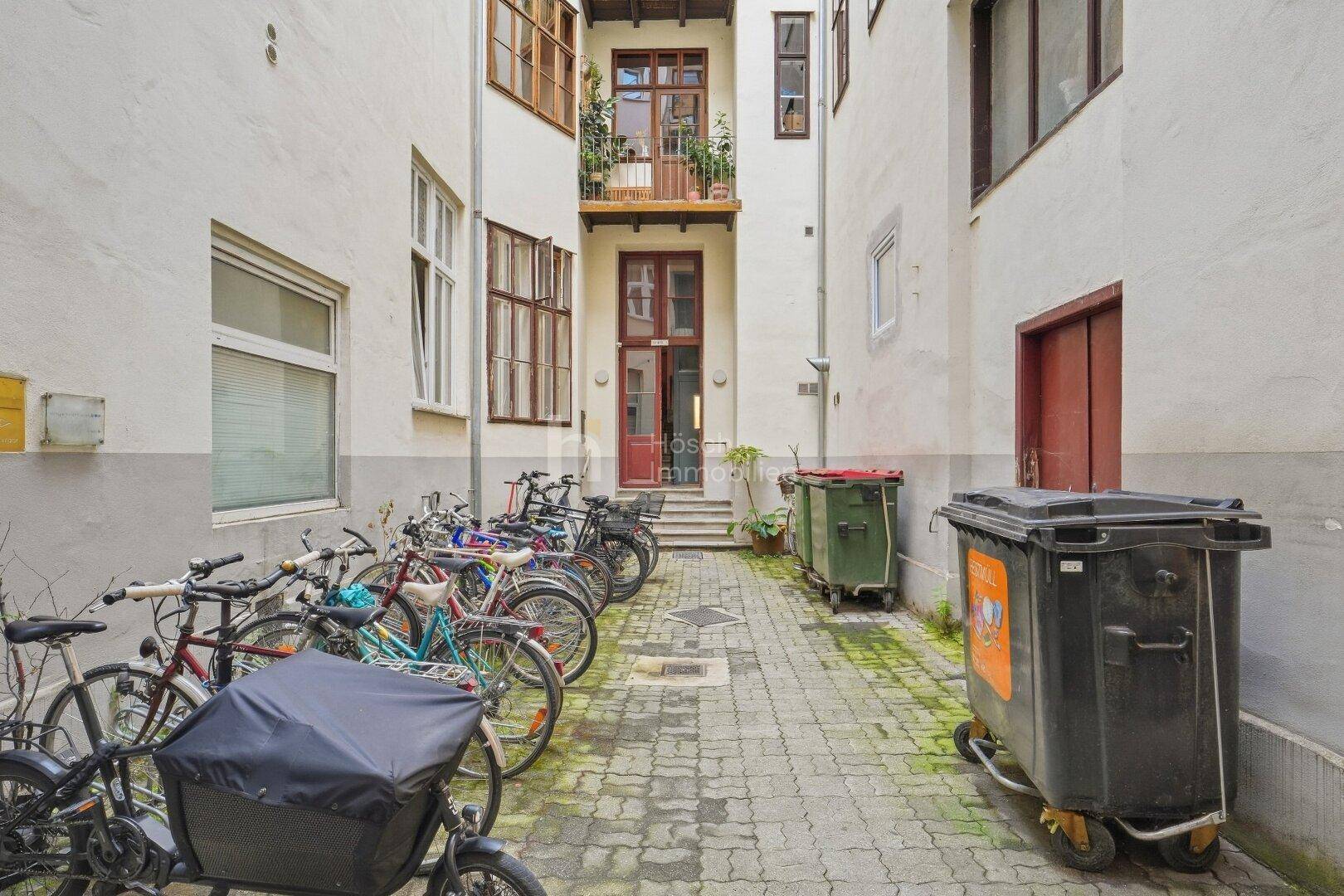 Detailansicht des Innenhofs mit zahlreichen Fahrrädern und Mülltonnen entlang der gepflasterten Fläche.