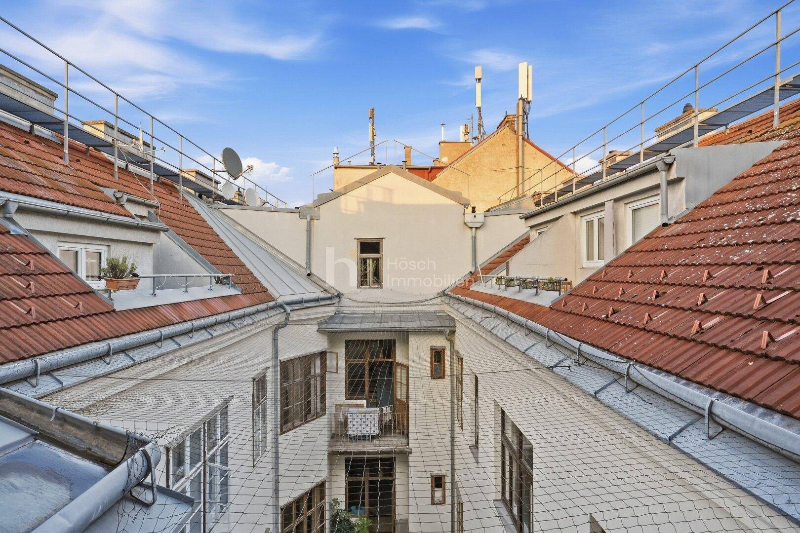 Blick von oben auf einen Innenhof mit roten Ziegeldächern und einem kleinen Balkon.