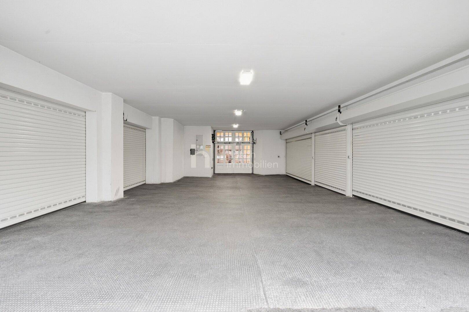 Geräumige Tiefgarage mit mehreren Rolltoren und Betonboden für Fahrzeuge.