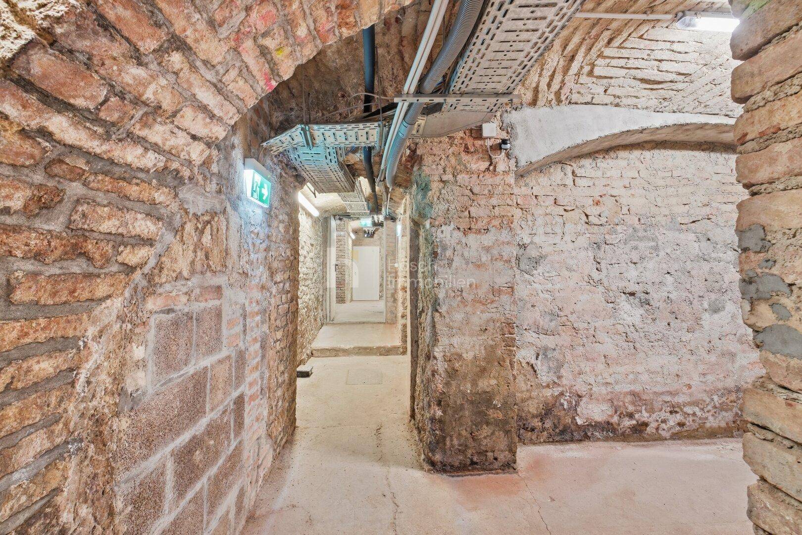 Historischer Kellergang mit freiliegenden Ziegelwänden, Gewölbedecken und sichtbaren Installationen.