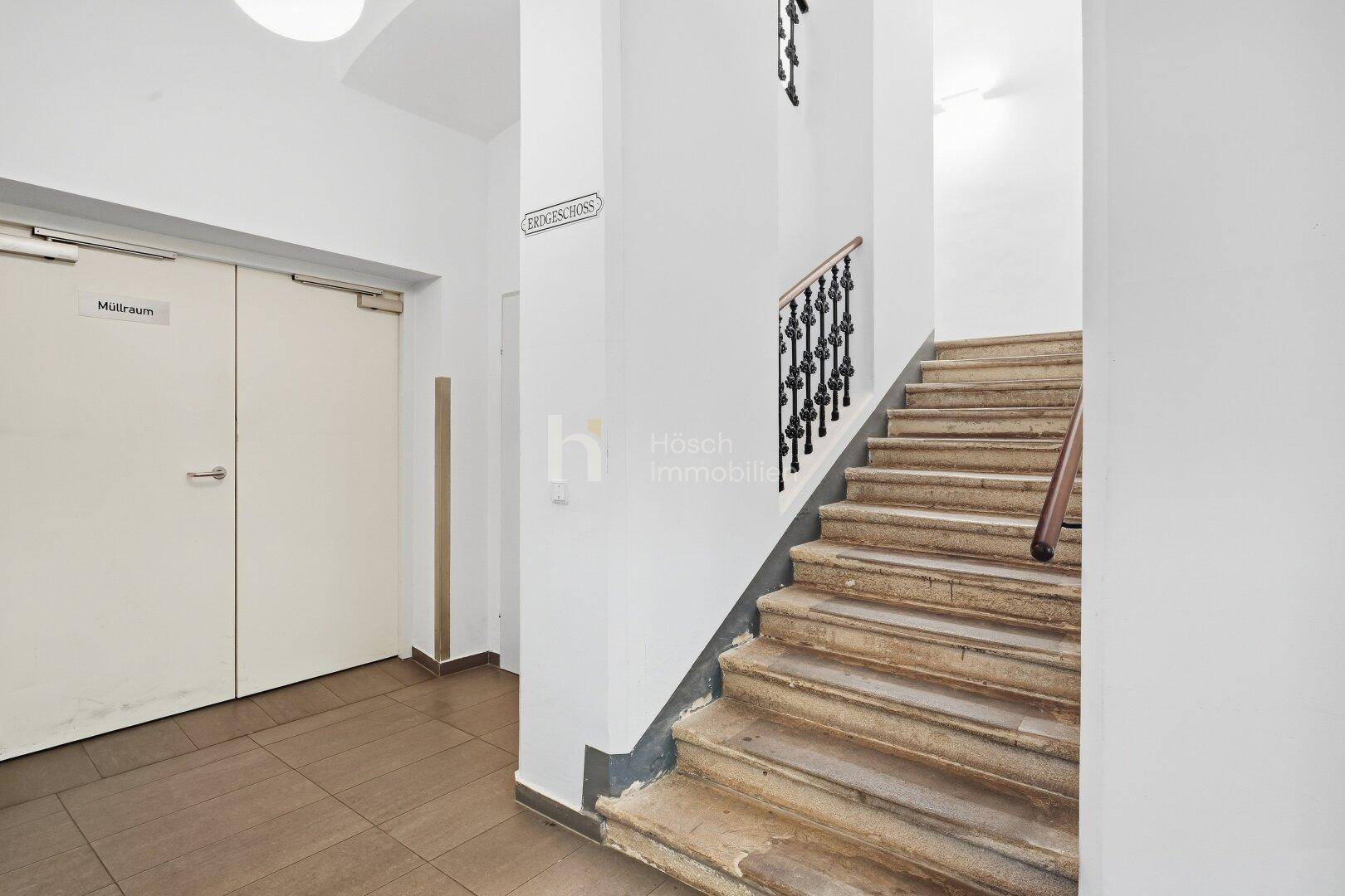 Altes Treppenhaus mit Steinstufen und schmiedeeisernem Geländer, Zugang zum Müllraum.