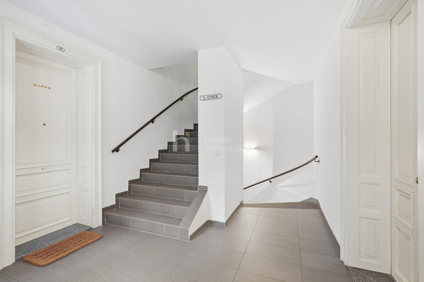 Modernisiertes Treppenhaus mit grauen Fliesenstufen und schlichtem schwarzem Geländer.
