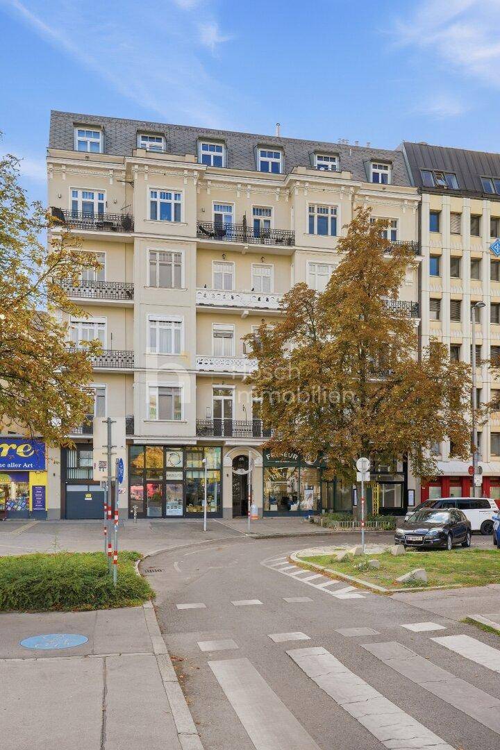 Historisches Gebäude mit detailreicher Fassade und Mansarddach, umgeben von Bäumen und städtischem Leben.