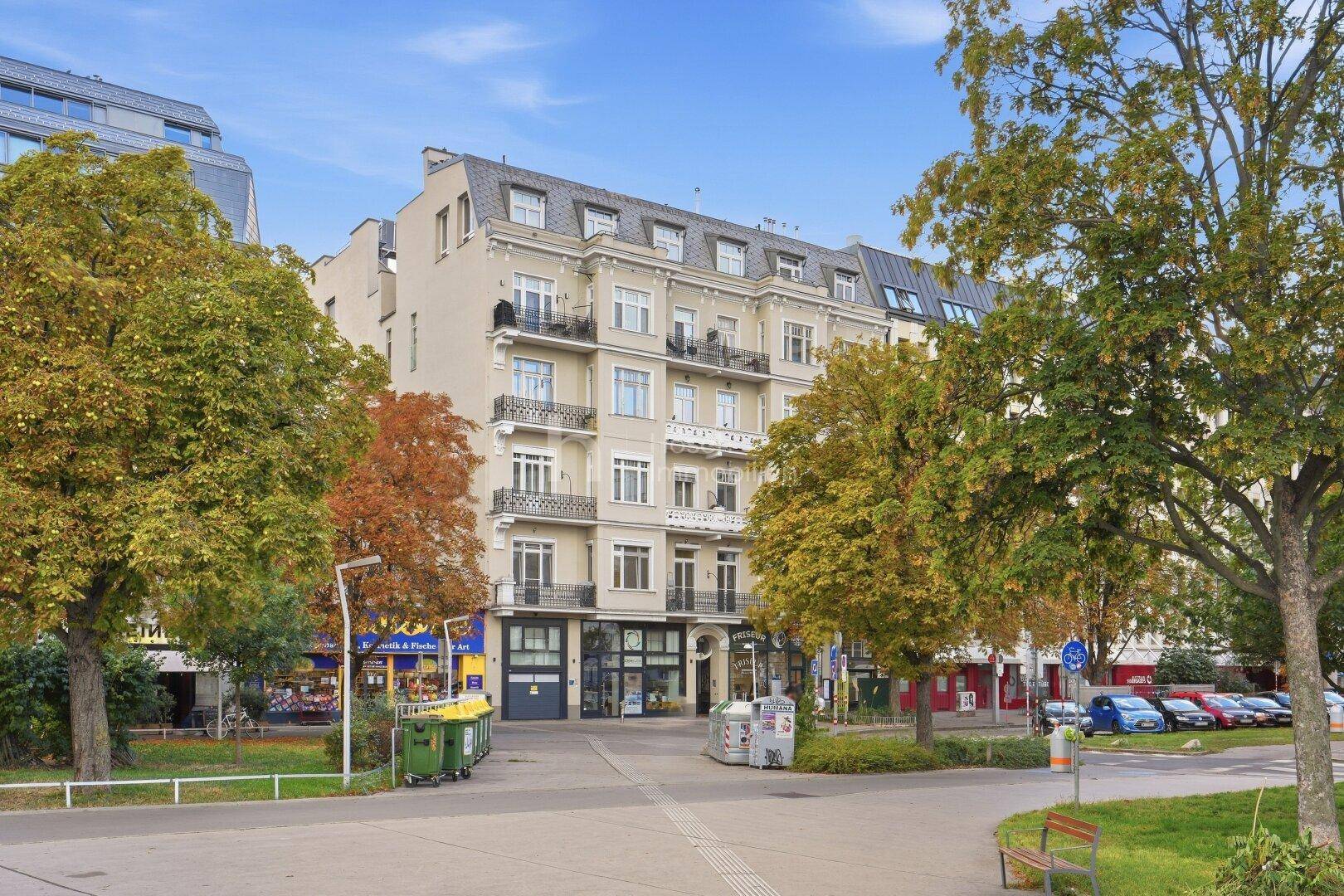 Historisches Gebäude mit eleganter Fassade und Mansarddach, eingebettet in eine grüne Stadtlandschaft.