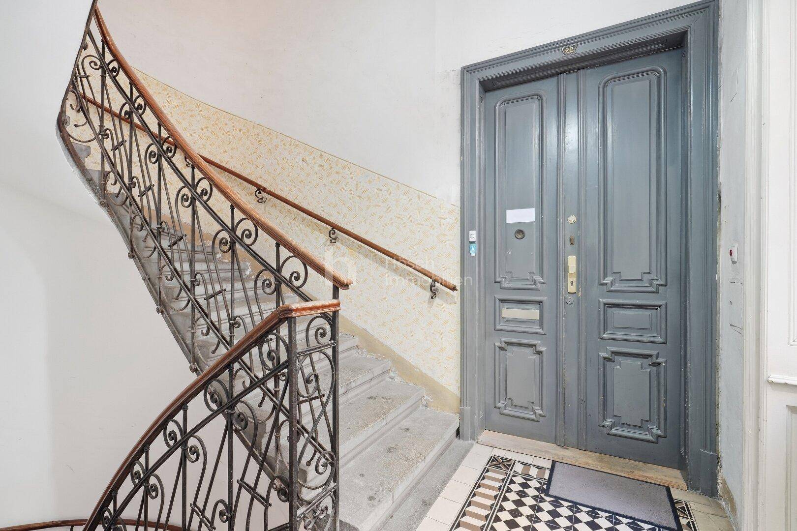 Historisches Treppenhaus mit schmiedeeisernem Geländer, Steinstufen und einer eleganten Wohnungstür.