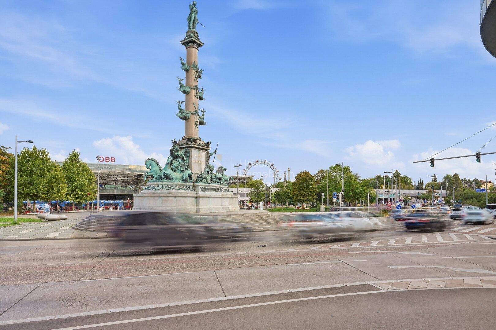 Weitläufige Stadtansicht mit einem imposanten Denkmal und dem Riesenrad unter blauem Himmel.