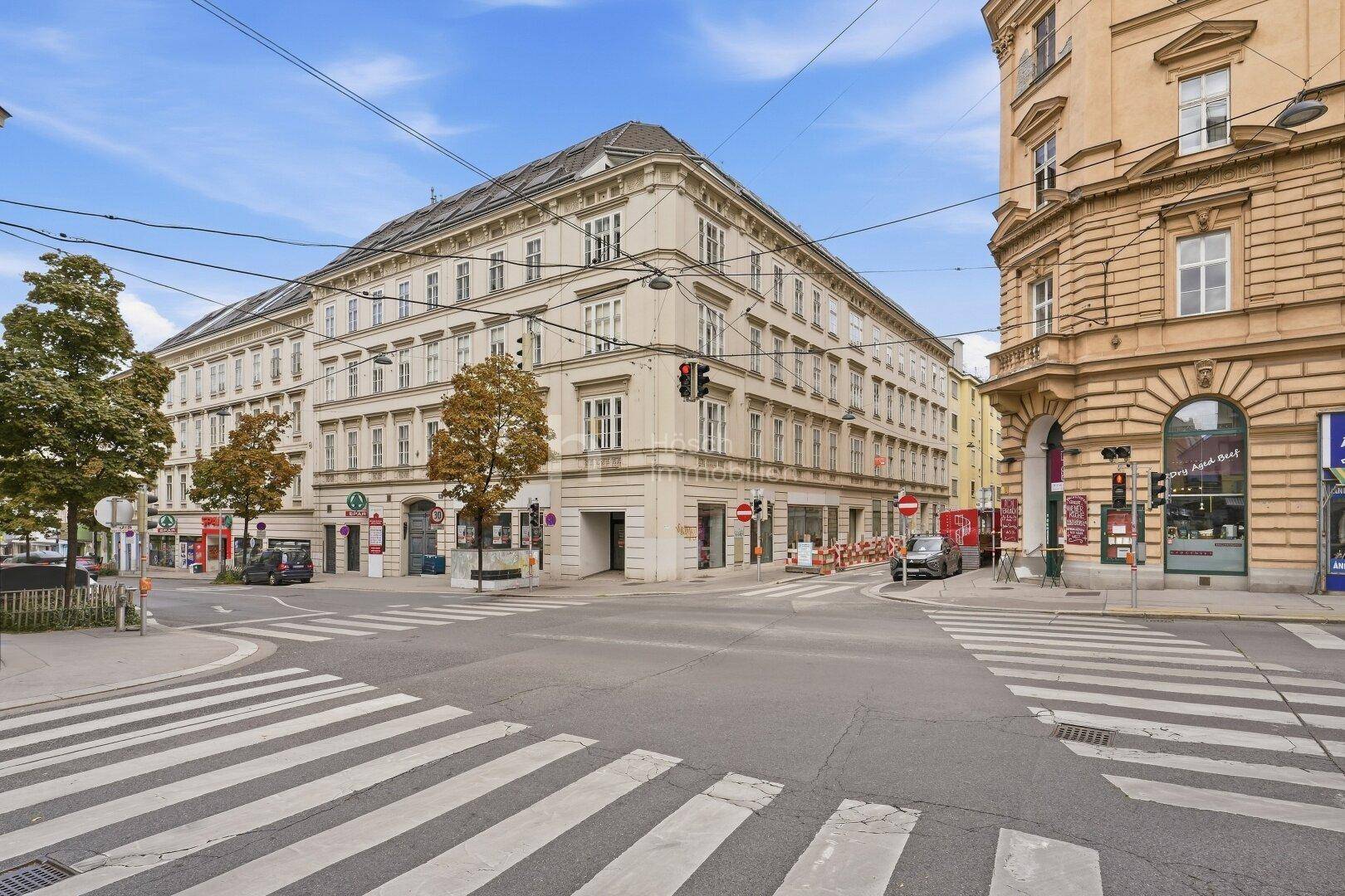 Großes Eckgebäude in urbaner Umgebung mit klassischer Architektur und Geschäften im Erdgeschoss.