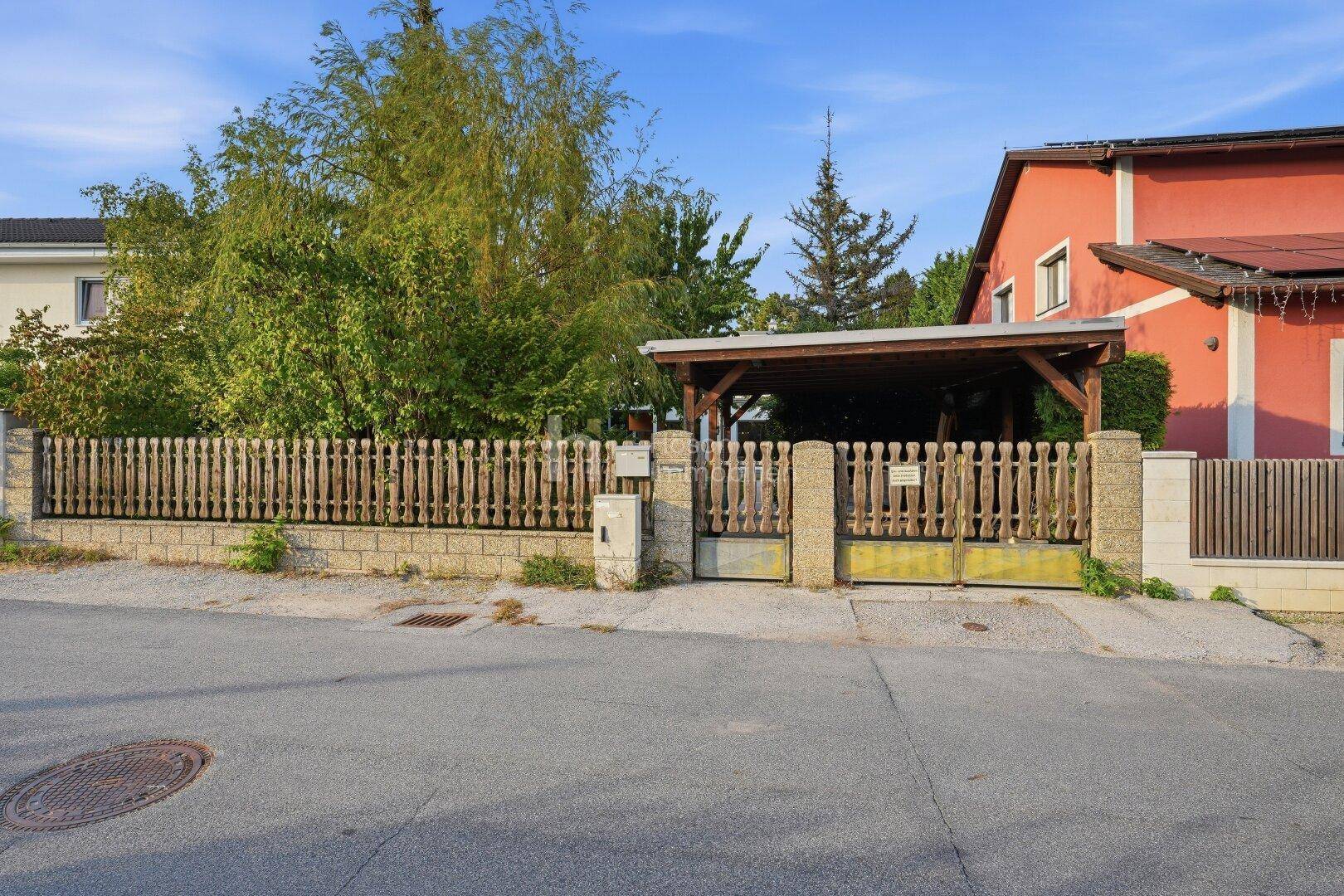 Eingangsbereich des Hauses mit Holzzaun, Carport und Zufahrt von der Straße.