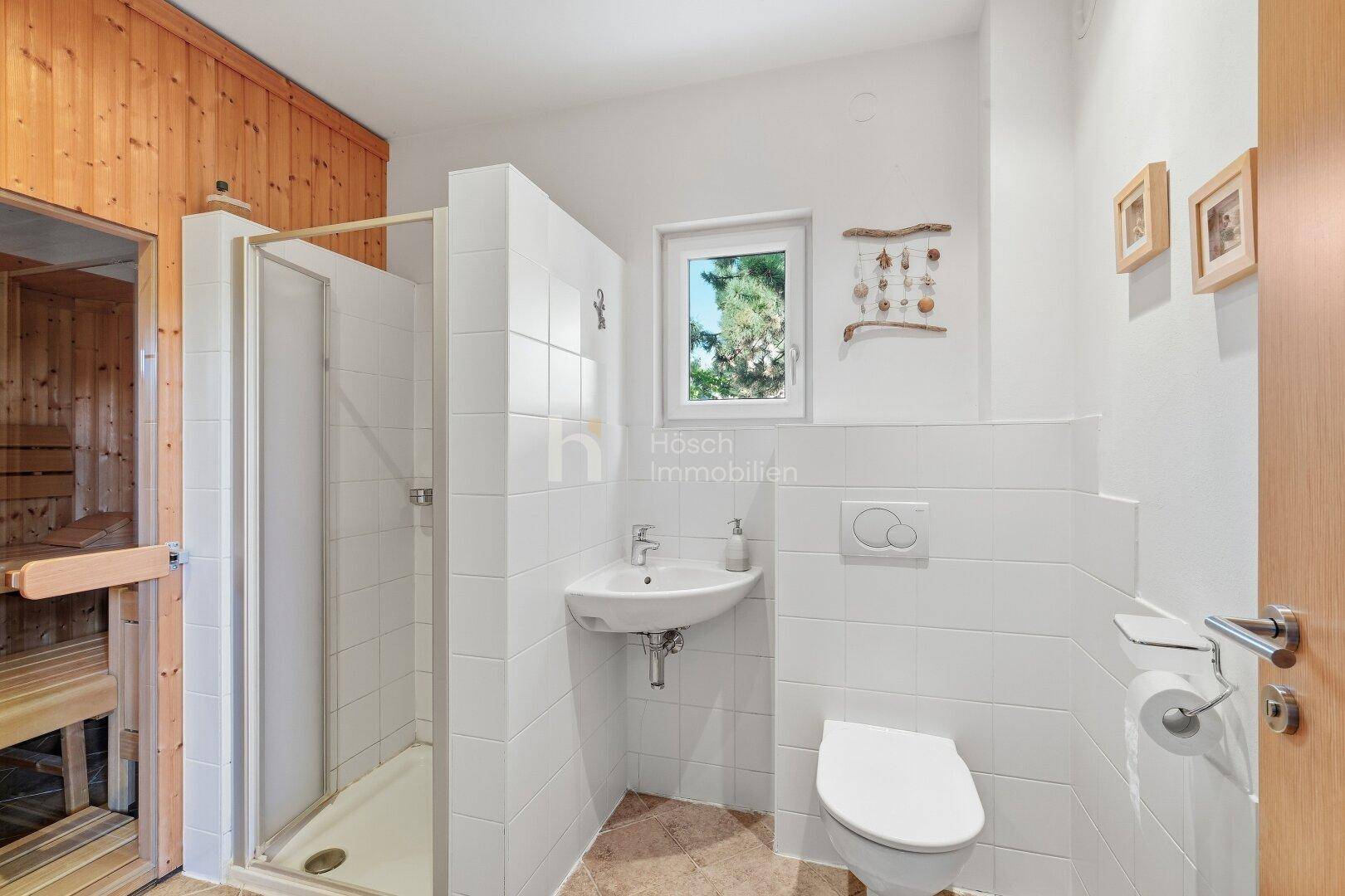 Badezimmer mit Dusche, WC, Waschbecken und Fenster, angrenzend an die Sauna.
