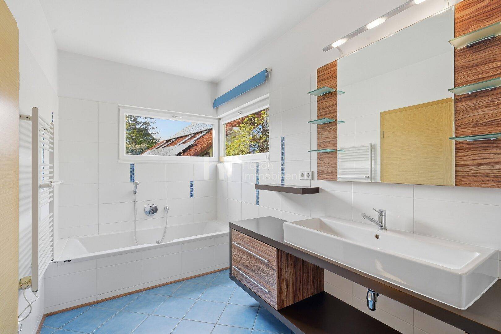 Modernes Badezimmer mit weißen Wandfliesen, blauen Bodenfliesen, Badewanne und Fenster.