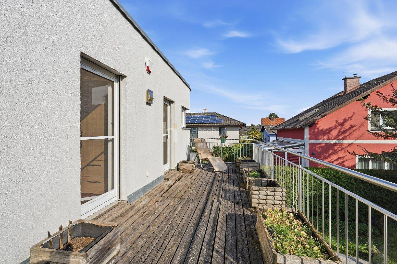 Großer Balkon mit Holzbelag, Metallgeländer und Blick auf die Nachbarschaft.