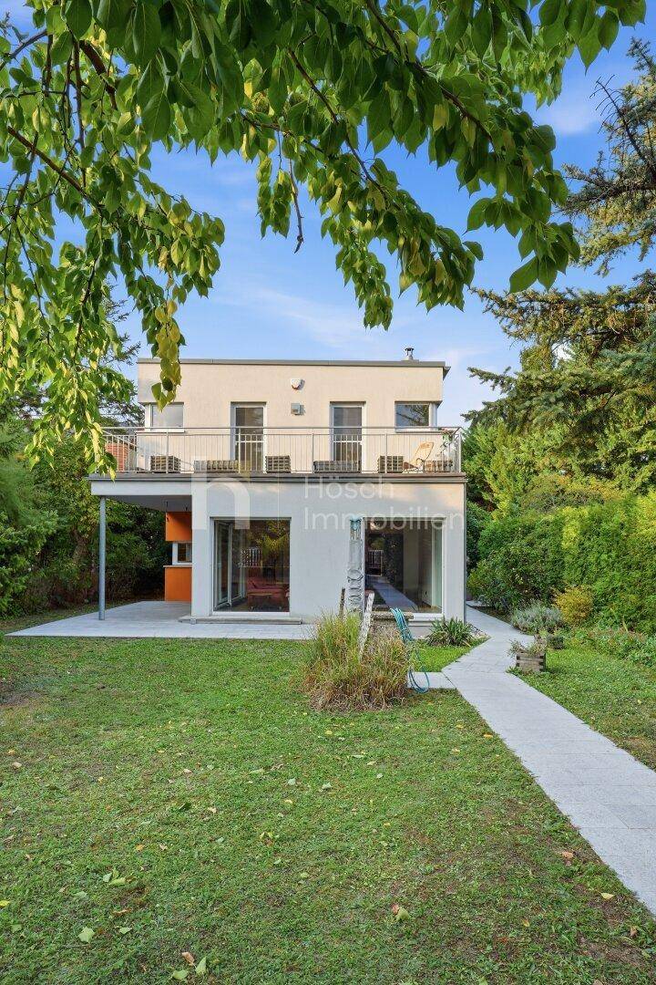 Modernes Haus mit Garten, großen Glasfronten und einem Balkon im Obergeschoss.
