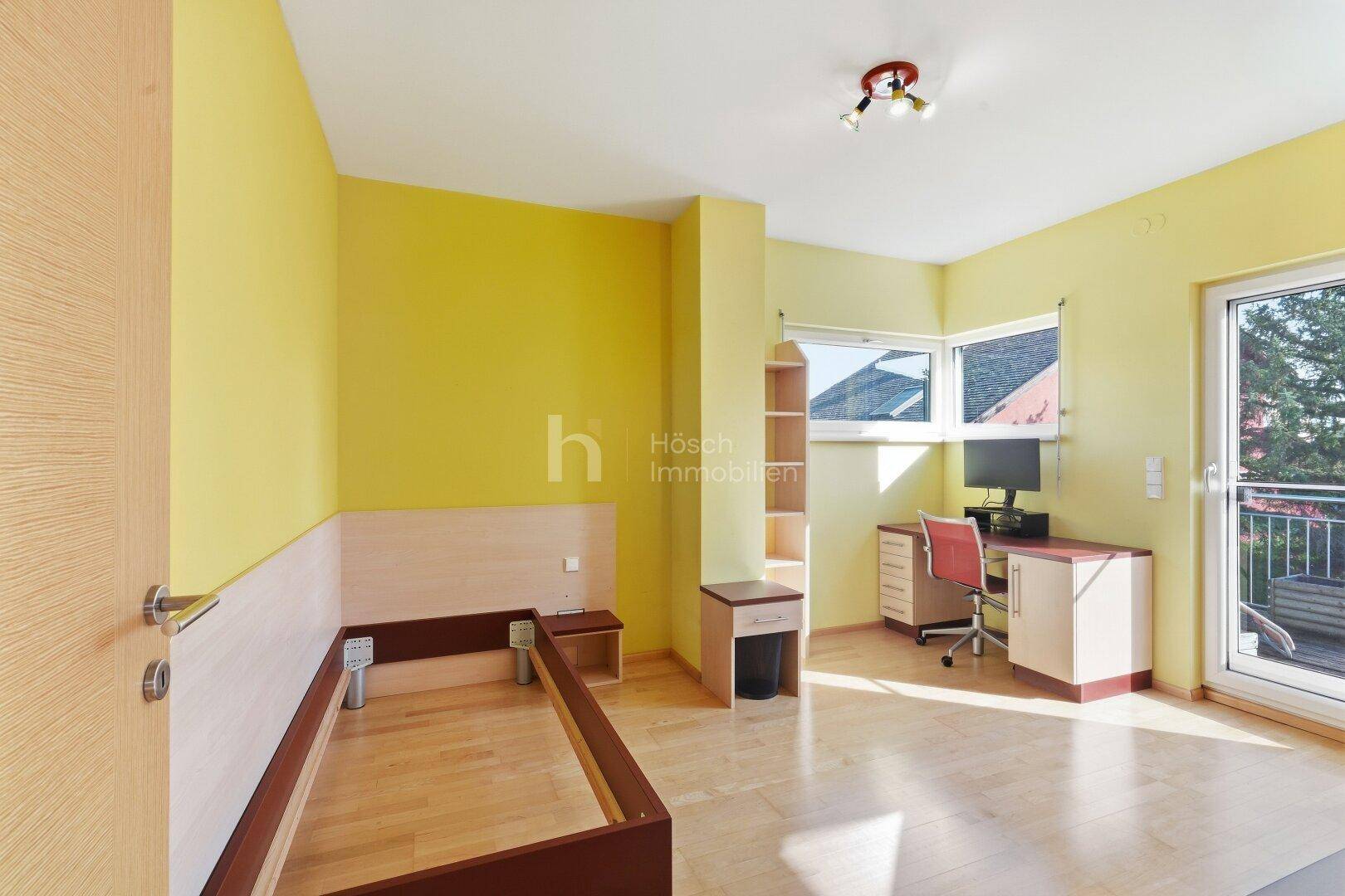 Helles Schlafzimmer mit gelben Wänden, Holzboden und direktem Zugang zum Balkon.