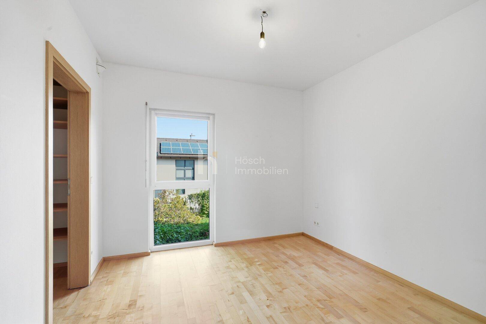 Heller Raum mit Holzboden, weißen Wänden und Zugang zu einem Außenbereich.