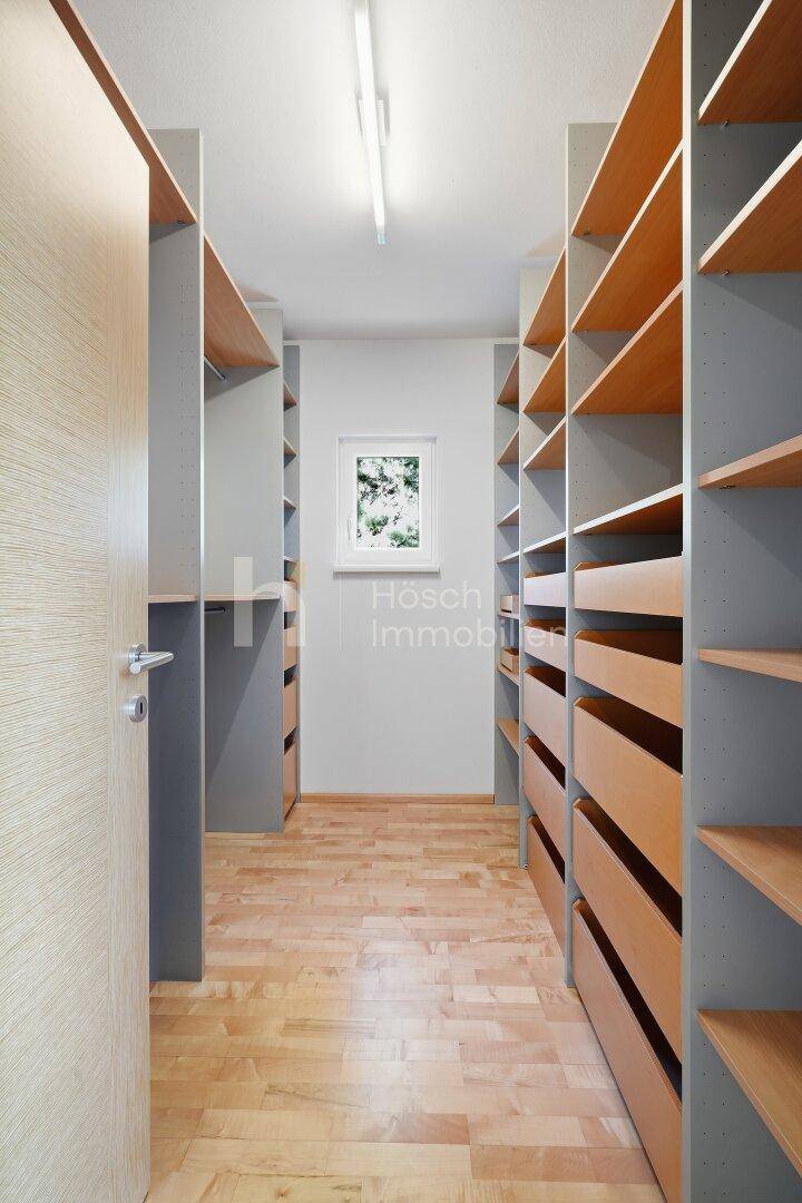 Geräumiger begehbarer Kleiderschrank mit maßgefertigten Regalen und Schubladen aus Holz.