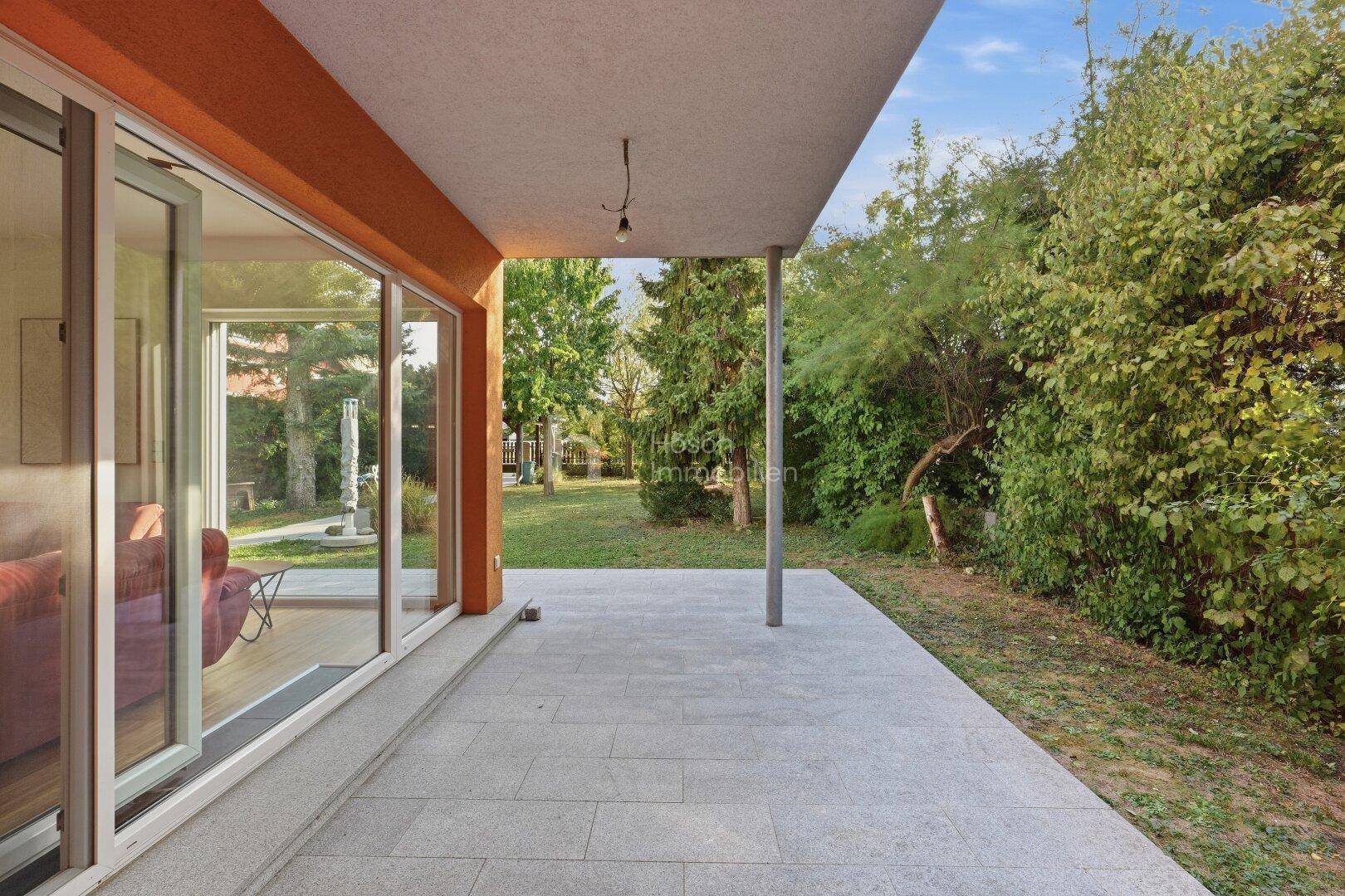 Großzügige, überdachte Terrasse mit Fliesenboden und direktem Zugang zum grünen Garten.