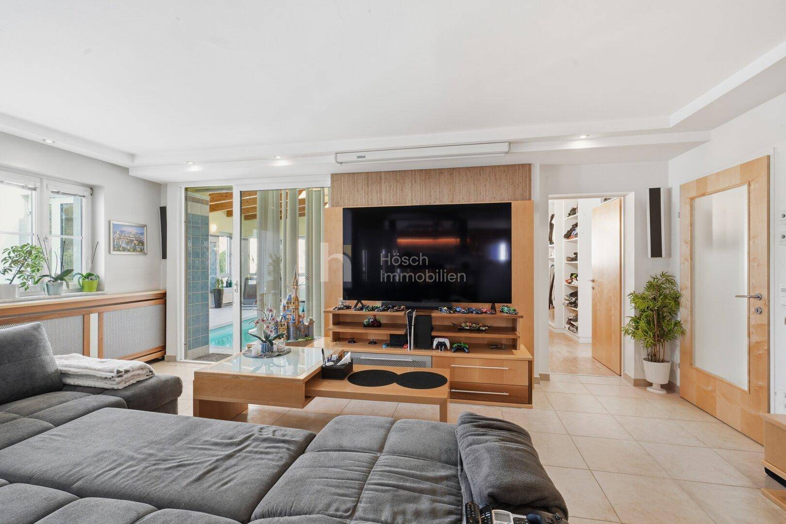 Helles Wohnzimmer mit großem Sofa, Entertainment-System und Zugang zum Außenbereich mit Pool.