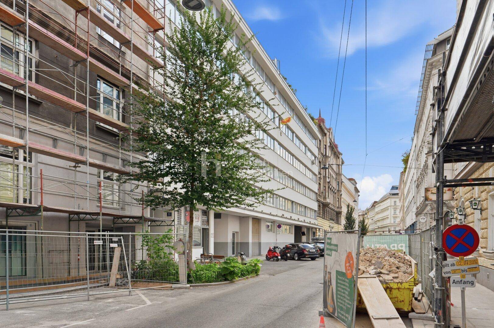 Straßenansicht mit einem modernen Gebäude und einem angrenzenden Gebäude unter Gerüst.