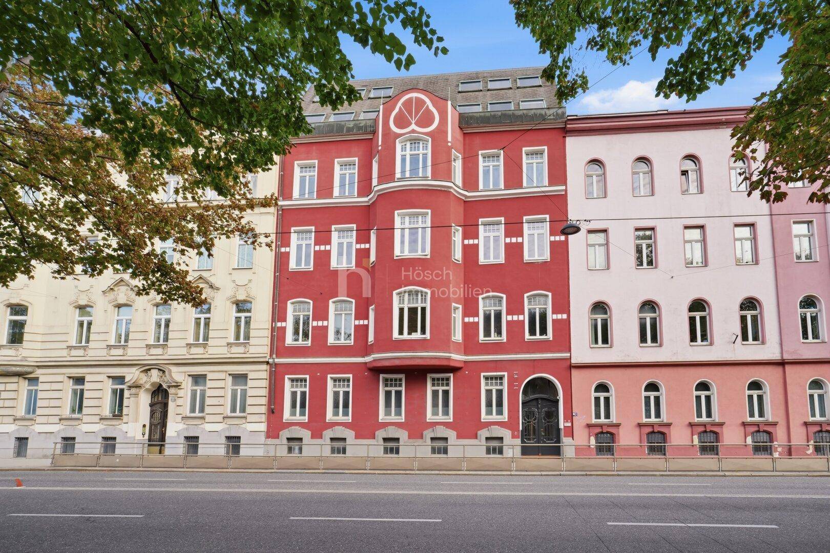 Historisches Gebäude mit markanter roter Fassade und vielen Fenstern an einer Stadtstraße.