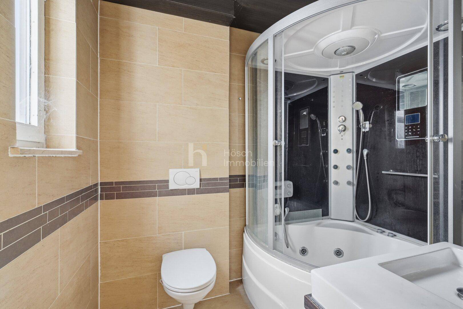 Badezimmer mit beiger Fliesenwand, Toilette und einer Duschkabine mit integrierter Badewanne.