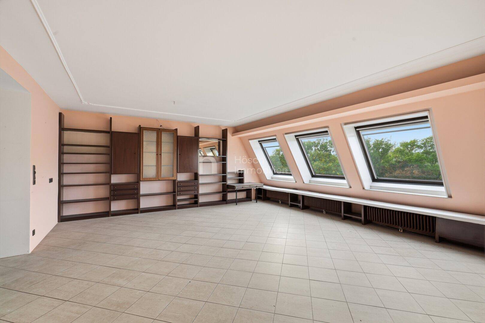 Geräumiger Wohnraum mit Fliesenboden, Dachfenstern und eingebauten Regalen, ideal für Bücherliebhaber.