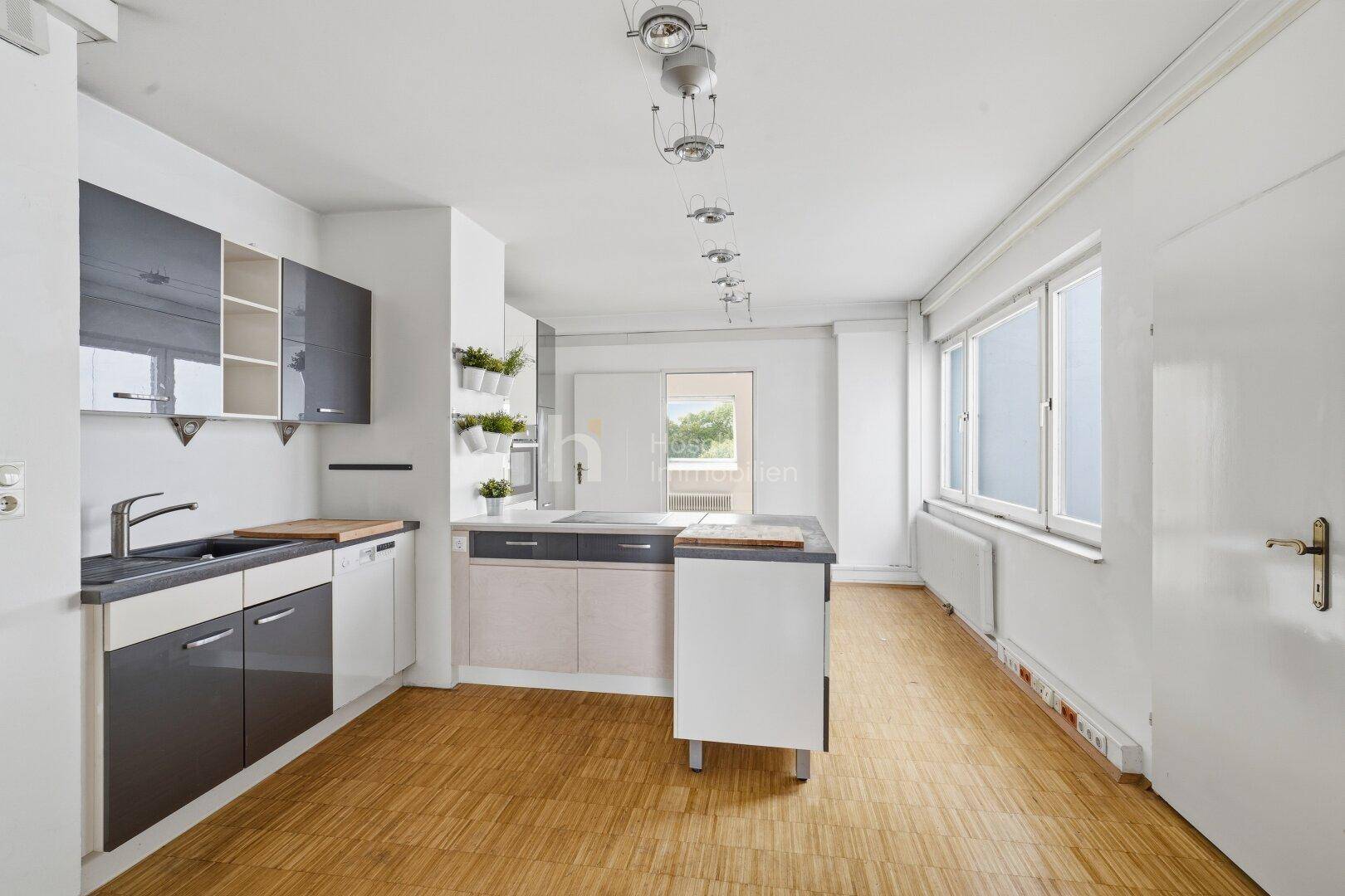 Moderne Küche mit grauen und weißen Schränken, Holzarbeitsplatten und viel Tageslicht.