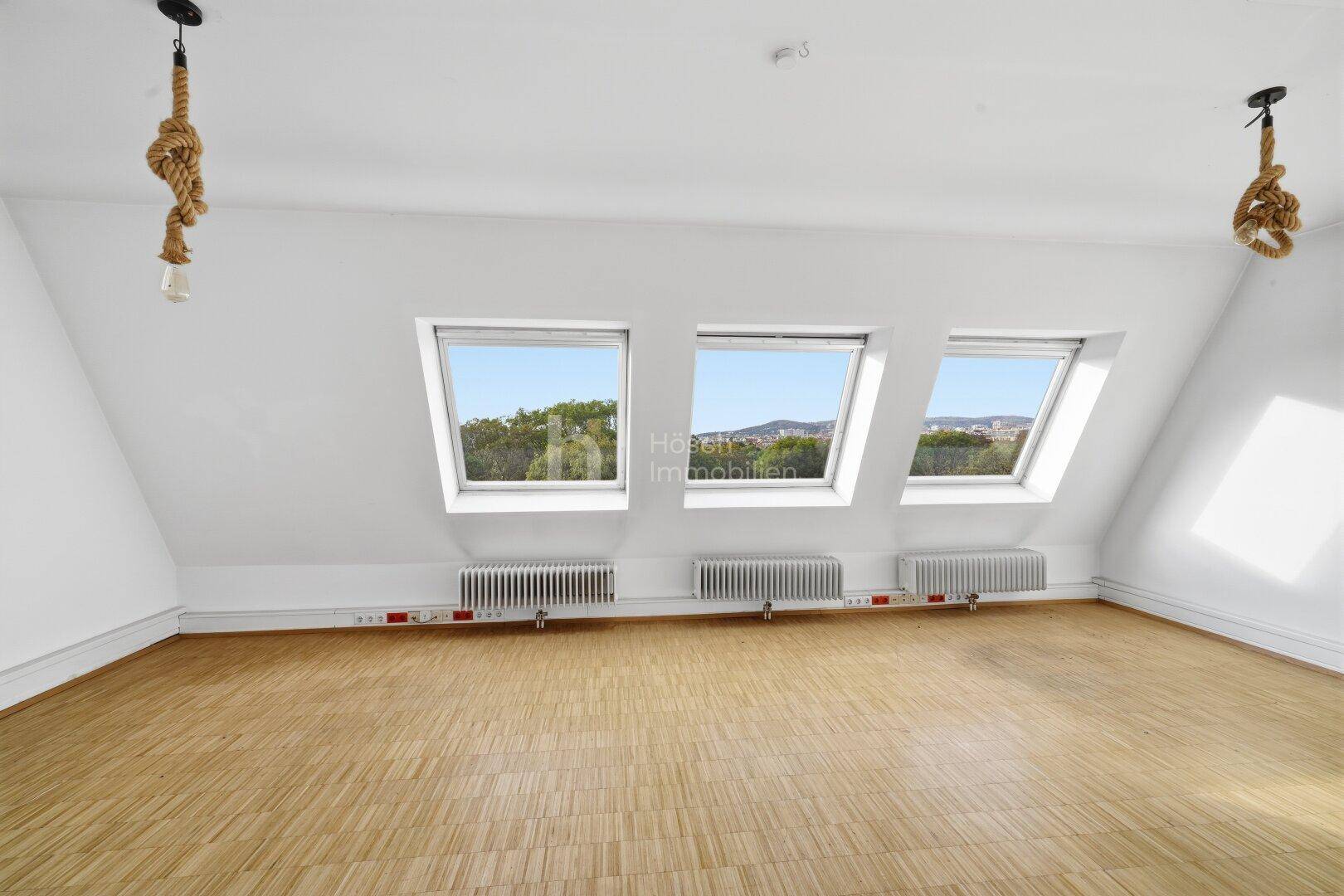 Dachgeschosszimmer mit schrägen Wänden, Dachfenstern und Blick ins Grüne.