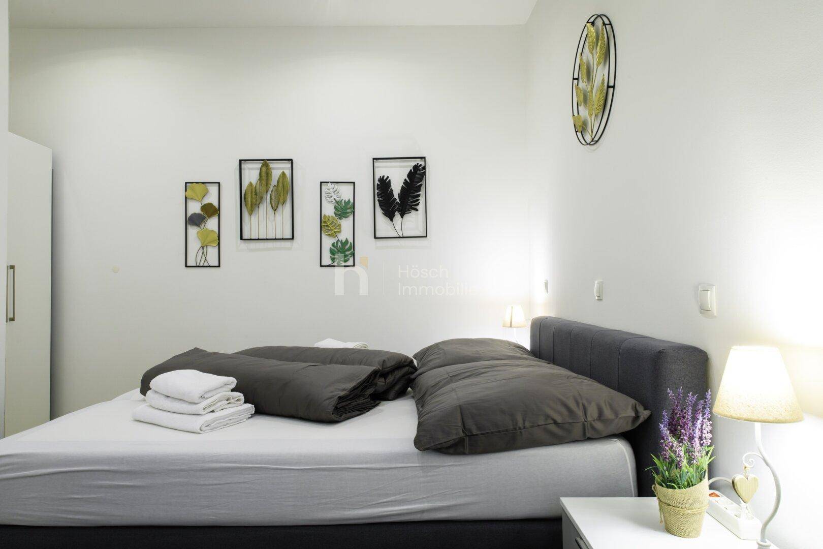 Schlafzimmer mit Doppelbett, Nachttisch und moderner Wanddekoration in hellen Farben.