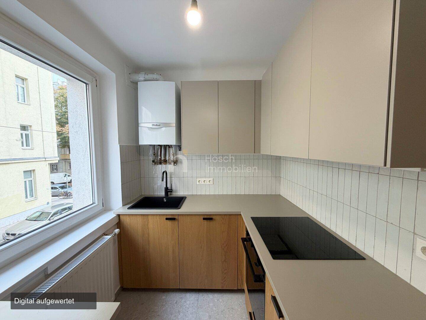 Moderne Küche mit hellen Schränken, Holzfronten und Induktionskochfeld unter dem Fenster.