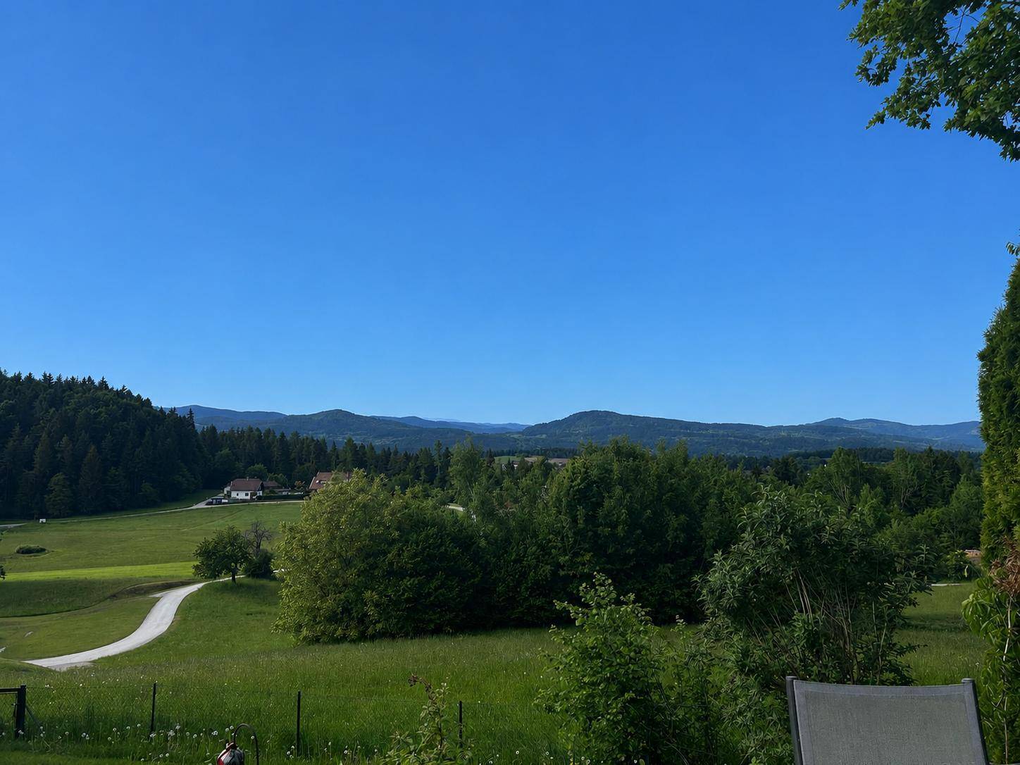 Malerische Aussicht auf weite grüne Felder und bewaldete Hügel unter einem klaren blauen Himmel.