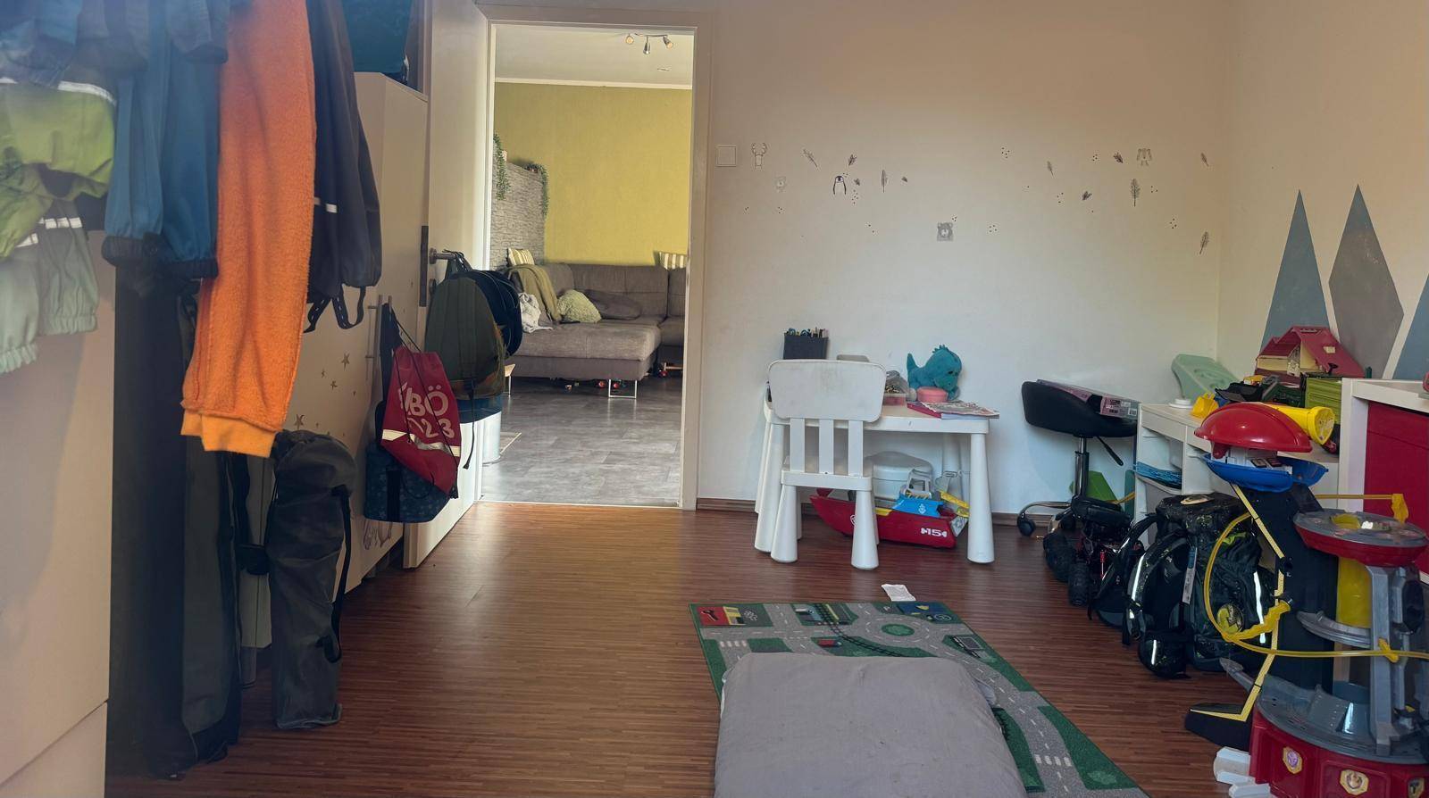 Kinderzimmer mit Kleiderstange, Spielbereich und Zugang zu einem weiteren Zimmer.